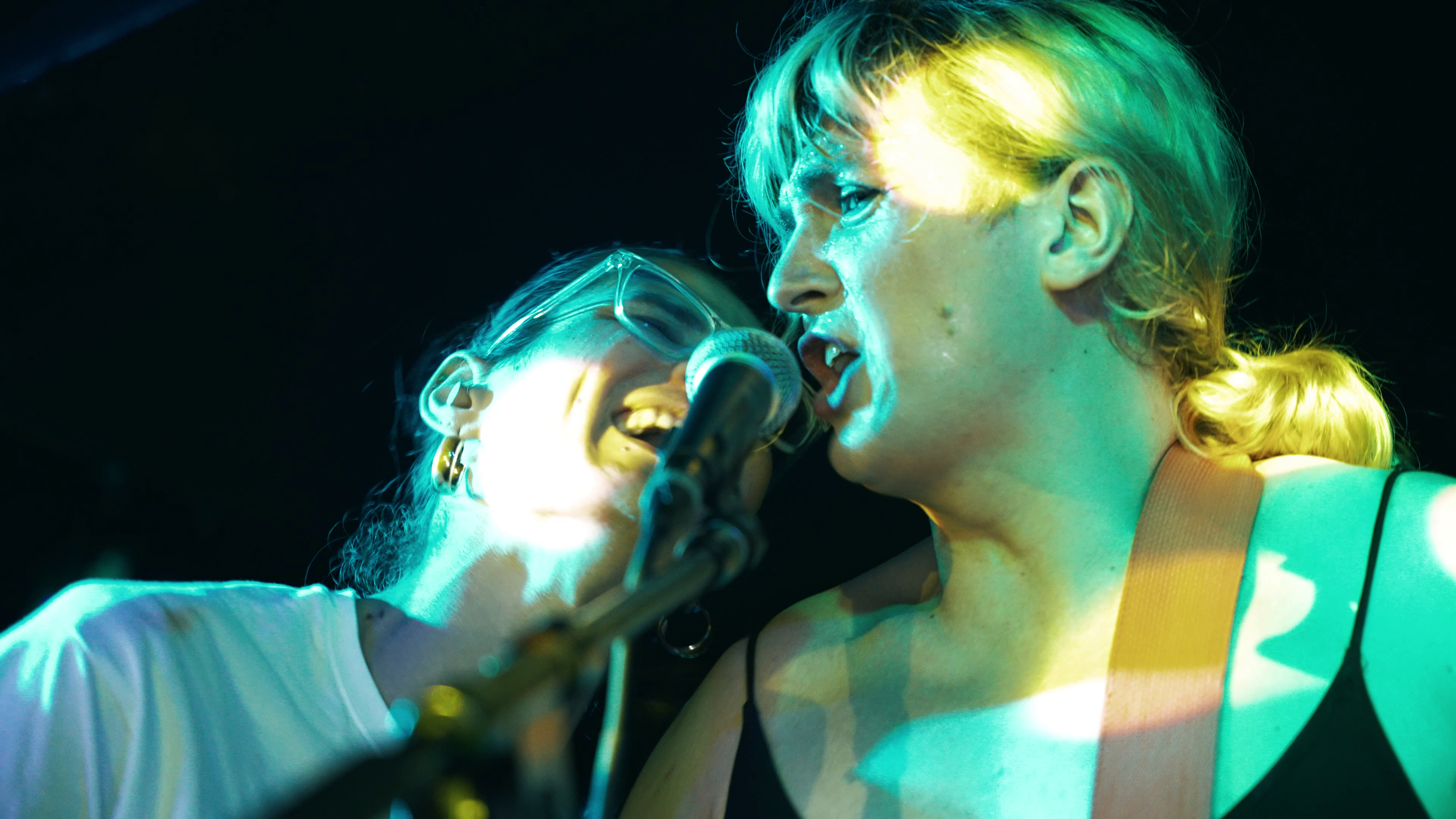 Two singers share a microphone under green and gold stage light