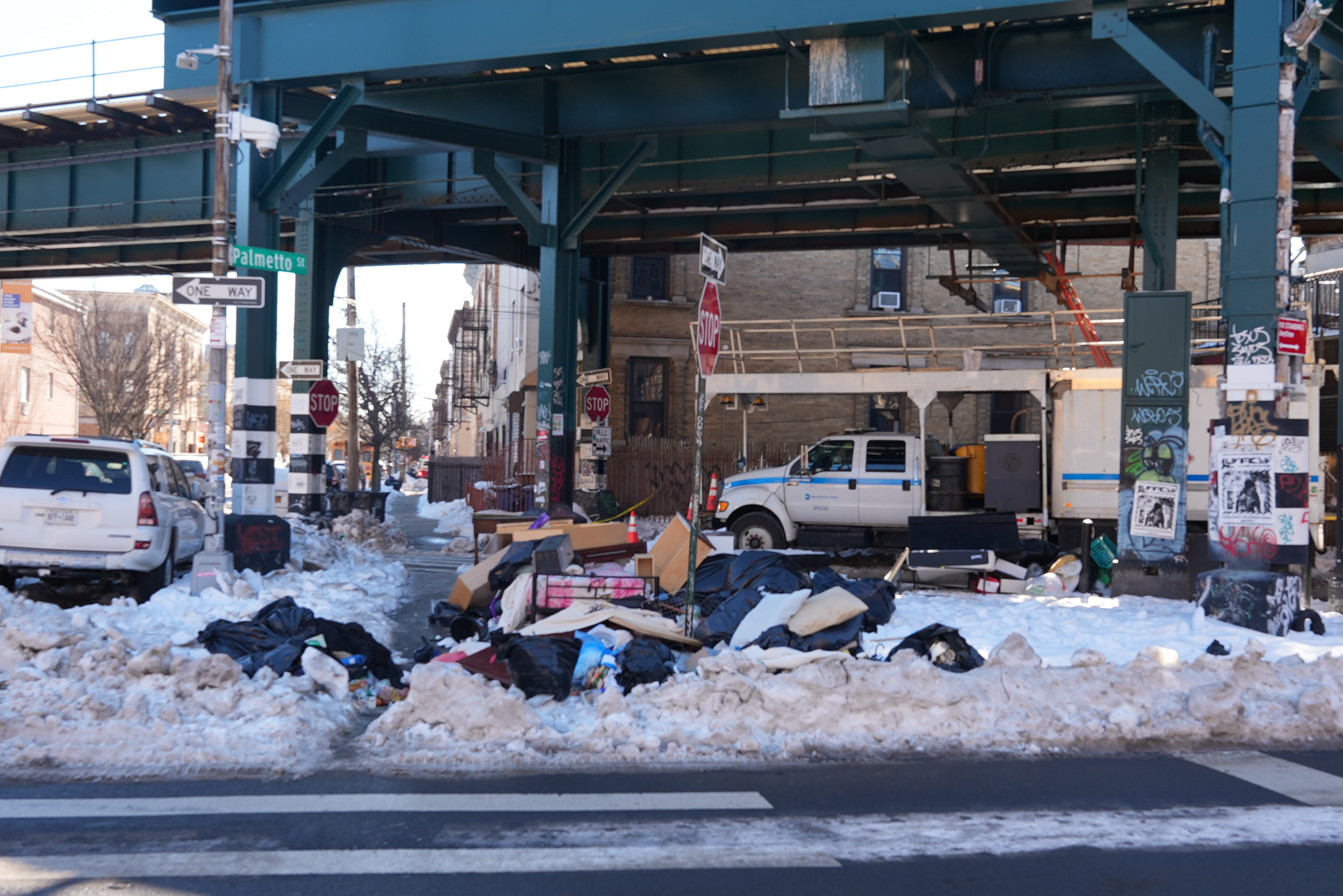 Dumped furniture and trash bags piled in snow beneath the elevated train