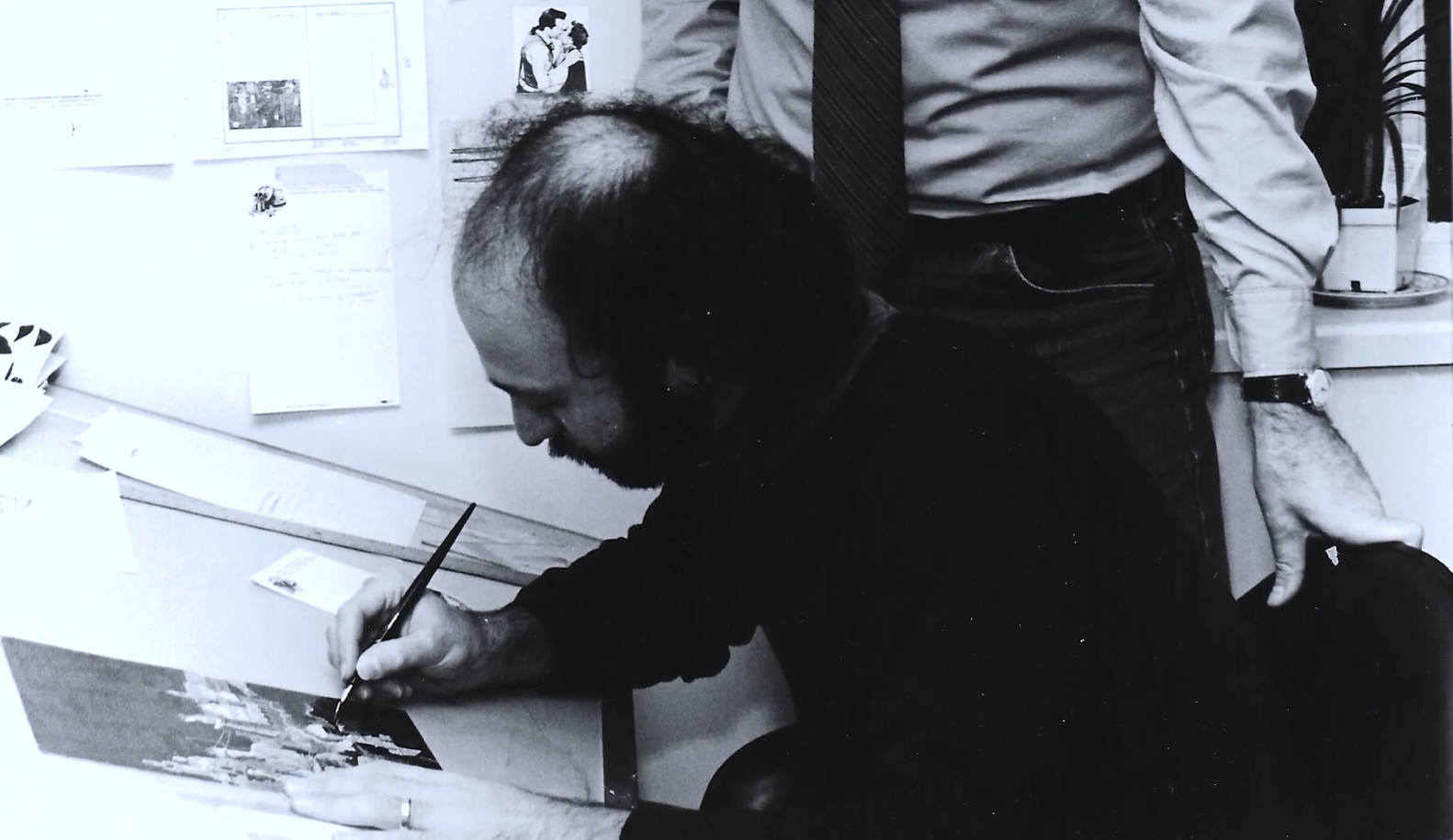 Archival photograph of a man leaning over a desk, retouching artwork with a fine brush